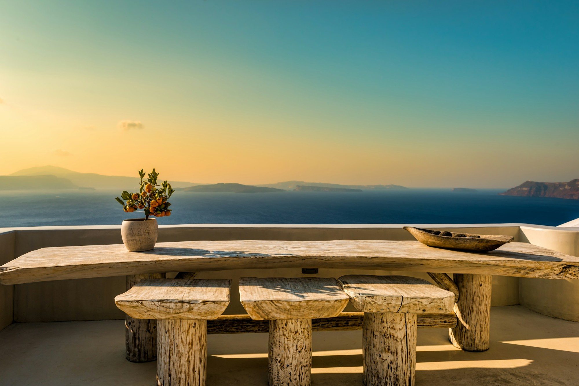 A driftwood table and stools on a terrace above the sea at sunset